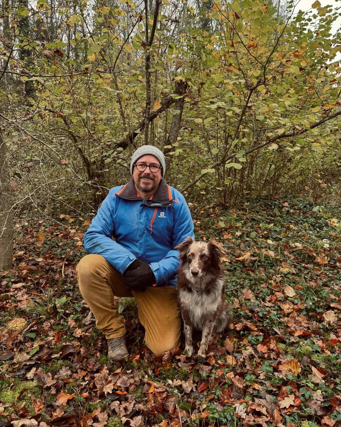 Ein Hundeführer kniet neben seinem Rettungshund im herbstlichen Wald